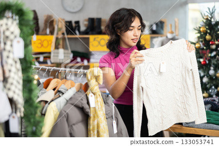 Young Filipino woman choosing sweaters in a store against the background of a Christmas tree 133053741
