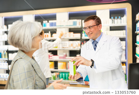Man apothecary hold package with cream and talks with senior woman client about nuances of care 133053760