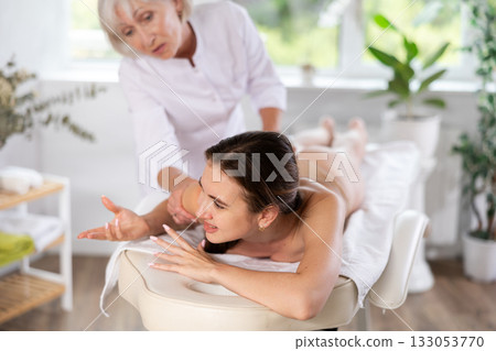 Young woman suffers painful sensations and winces during therapeutic massage session Young woman suffers painful sensations and winces during therapeutic massage session 133053770