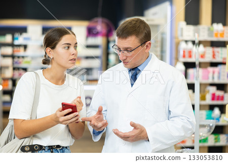 Pharmacist man communicates with girl client, looks at mobile phone screen 133053810