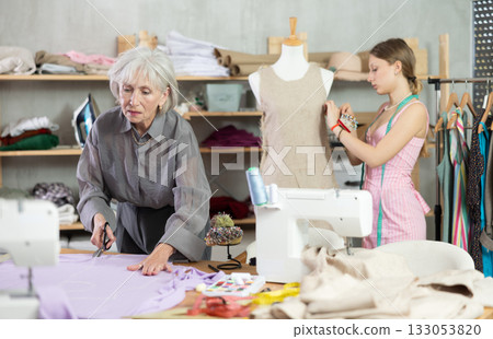 Elderly woman cutting fabric female assistant sews on mannequin Elderly woman cutting fabric female assistant sews on mannequin 133053820