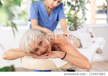 Aged woman relaxing in spa center during professional back massage 133053861