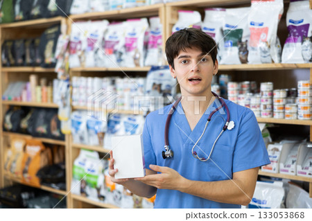 Experienced veterinarian young man is standing in pet store with pack of food in hands Experienced veterinarian young man is standing in pet store with pack of food in hands 133053868