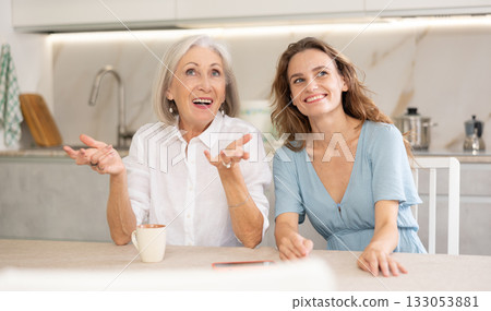 Elderly mother and adult daughter drinking tea and chatting happily Elderly mother and adult daughter drinking tea and chatting happily 133053881