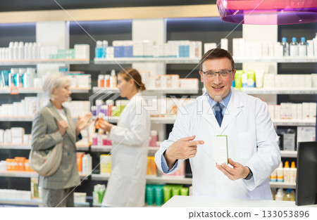 Middle-aged male pharmacist demonstrating preparation in box 133053896