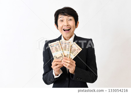 A smiling middle-aged woman in a suit holding a wad of bills and being surprised A smiling middle-aged woman in a suit holding a wad of bills and being surprised 133054216