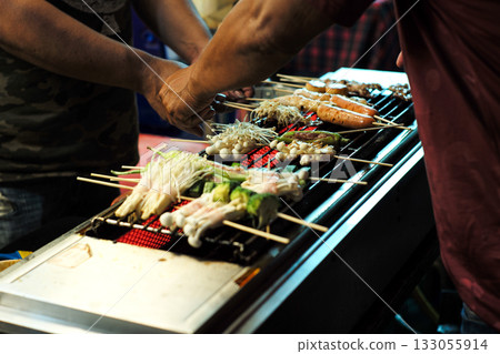 The hands of sellers grill the various types of food such as sauce, mushroom, chilli, pork, ham on the electrical stove in the night flea market 133055914