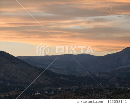 serene sunset bathed in pastel hues illuminates rolling hills and towering distant mountain peaks serene sunset bathed in pastel hues illuminates rolling hills and towering distant mountain peaks 133058141