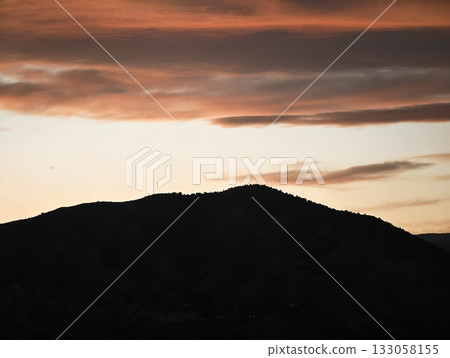 gloomy hill silhouette contrasted sharply against vivid orange and turbulent sky with distant birds 133058155