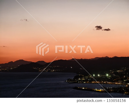 seaside horizon glows with activity, distant mountains stand against glowing sunset over tranquil 133058156
