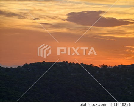 evening sunset view, calm twilight scene featuring illuminated clouds above gentle hill silhouettes 133058256