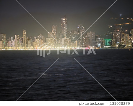 nighttime cityscape with reflections, illuminated shoreline city with vibrant reflections and towers 133058279