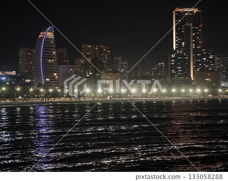 seaside luminance vibe, coastal promenade shimmering under neon lights with relaxing nighttime 133058288