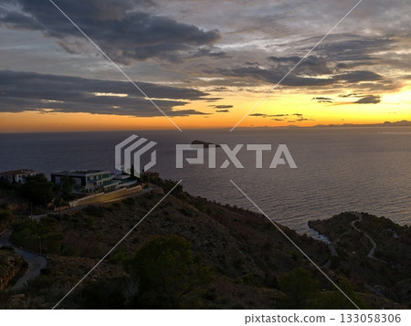 peaceful seaside cliff view at dusk, calm coastal evening with warm villa lights and misty horizon 133058306