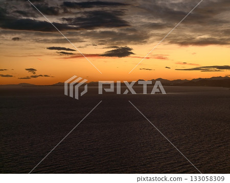 calm maritime scene at dusk, serene horizon bathed in amber light reflecting on gentle waves 133058309