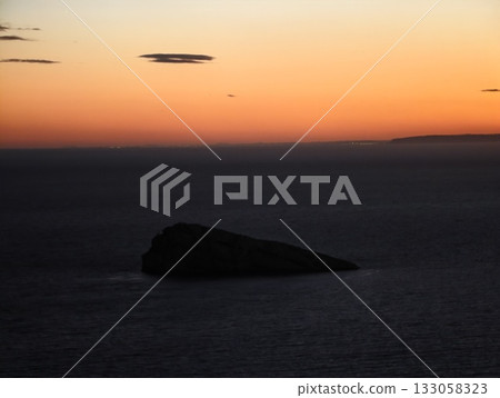 serene island against glowing sky, quiet silhouette of island at sunset with calm ocean background serene island against glowing sky, quiet silhouette of island at sunset with calm ocean background 133058323