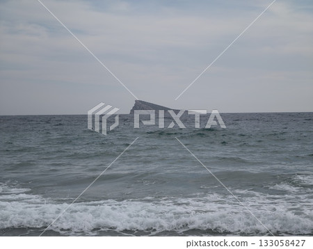 isolated triangular islet amidst stormy waters, secluded triangular rock surrounded by turbulent 133058427