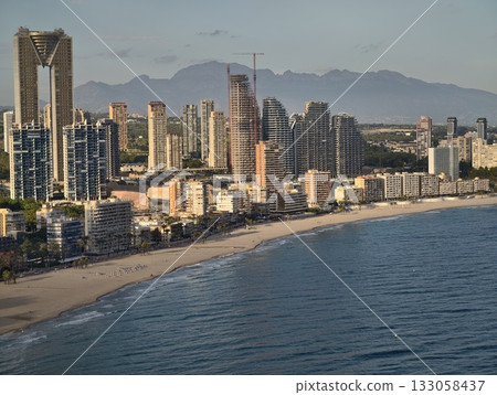bright sunset illuminates modern skyline with waves and mountain backdrop along busy shoreline 133058437