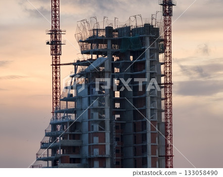 urban construction scene, city skyline behind partially built tower with construction equipment 133058490