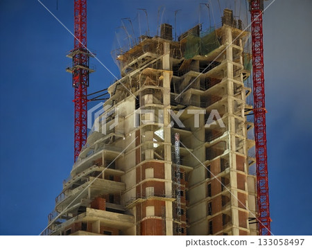 building illuminated with heavy equipment, nighttime construction site featuring scaffolding 133058497