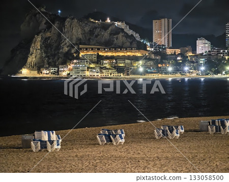 serene coastal scene, peaceful nocturnal beach setting featuring gentle waves and city reflections 133058500