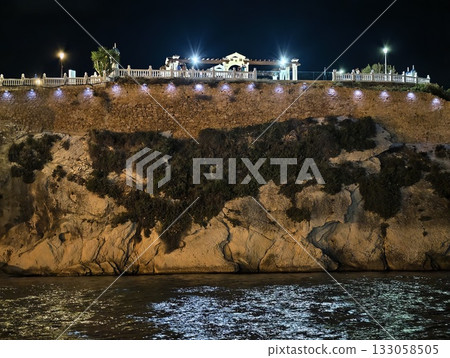 cliffside walkway with lights, coastal promenade at dusk with illuminated balustrade and calm waters 133058505