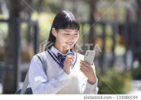 Smiling female high school student looking at smartphone screen 133060144