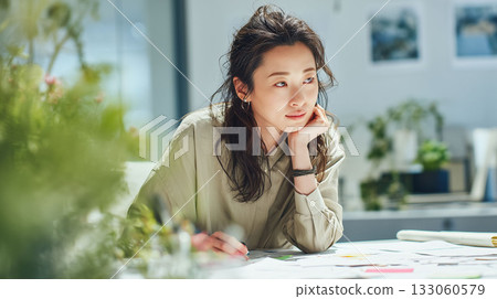 一位職業婦女在現代辦公室裡，對著文件沉思。畫面展現了她專注的神情，以及她伏案的場景。 133060579