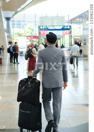Business traveler in smart suit walking through bustling airport terminal with suitcase in tow during the day Business traveler in smart suit walking through bustling airport terminal with suitcase in tow during the day 133062108
