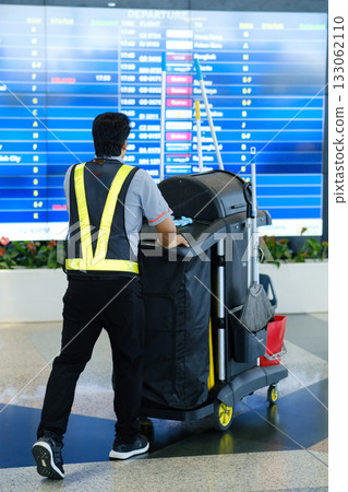 Janitor cleaning airport terminal while flight information displays are updated, showcasing the busy environment Janitor cleaning airport terminal while flight information displays are updated, showcasing the busy environment 133062110