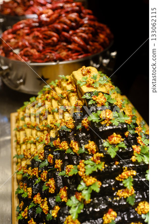Colorful and detailed pyramid of sushi decorated with herbs, showcasing culinary art at a lively food market during evening hours 133062115