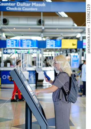 Woman using a self-service kiosk at a busy airport terminal during daytime to check in for her flight Woman using a self-service kiosk at a busy airport terminal during daytime to check in for her flight 133062129