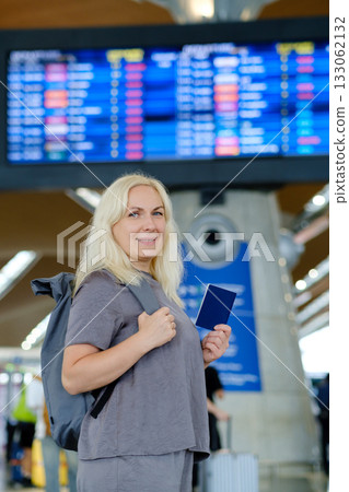 Woman at airport checking flight information while holding her passport and standing near departure board 133062132