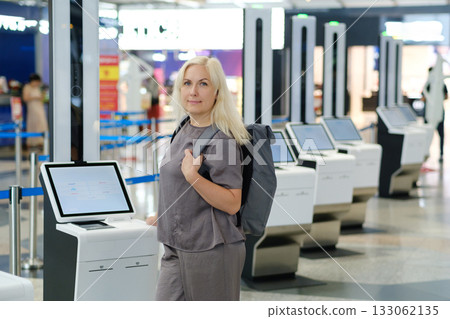 Woman with backpack interacting with check-in kiosk in modern airport terminal during busy travel season 133062135