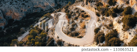 Winding mountain road amid trees and rugged cliffs from an aerial perspective 133063521