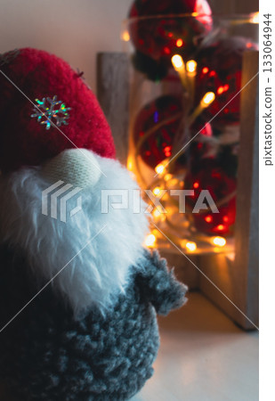 Scandinavian gnome with Christmas lights, vertical. Swedish Santa Claus and warm bulb garland, close up. Christmas decoration and toys. New Year mood. Festive illumination and Christmas gnome Scandinavian gnome with Christmas lights, vertical. Swedish Santa Claus and warm bulb garland, close up. Christmas decoration and toys. New Year mood. Festive illumination and Christmas gnome 133064944