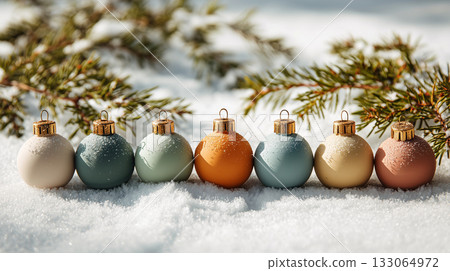 row of colorful Christmas ornaments sits in snow, surrounded by evergreen branches, creating festive and serene winter scene 133064972