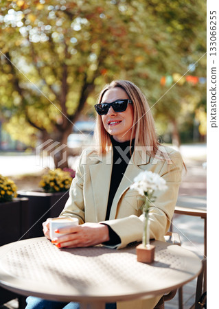 Woman enjoying coffee outdoors on a sunny day in a vibrant city setting 133066255
