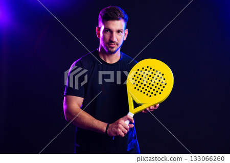 Man holding a yellow paddle racquet in a dimly lit studio with colorful lights Man holding a yellow paddle racquet in a dimly lit studio with colorful lights 133066260