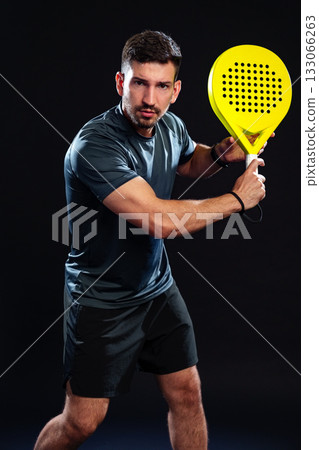 Man prepares to play padel in a professional setting with a vibrant yellow racket 133066263