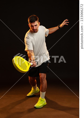 Man practicing paddle tennis indoors with a bright paddle and focused expression 133066272