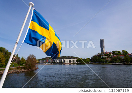 Swedish flag with colony of small wooden historic houses on the Slottsberget mountain with the tallest Scandinavian building Karlatornet skycraper in Lindholmen in background, Gothenburg, Sweden 133067119