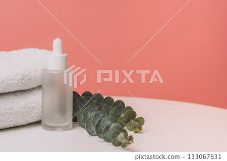Glass dropper bottle with eucalyptus and towels on pink background 133067831