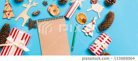 Top view of notebook on blue background made of Christmas decorations. New Year time concept Top view of notebook on blue background made of Christmas decorations. New Year time concept 133068064