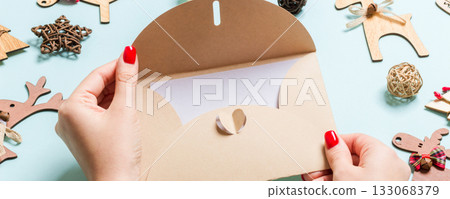 Top view of woman holding an envelope on blue background made of holiday decorations. Christmas time concept Top view of woman holding an envelope on blue background made of holiday decorations. Christmas time concept 133068379