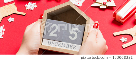 Top view of female hands holding calendar on red background. The twenty fifth of December. Holiday decorations. Christmas time concept Top view of female hands holding calendar on red background. The twenty fifth of December. Holiday decorations. Christmas time concept 133068381