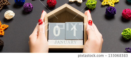 Top view of female hands holding calendar on black background. The first of January. Holiday decorations. New Year concept Top view of female hands holding calendar on black background. The first of January. Holiday decorations. New Year concept 133068383
