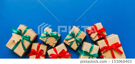wrapped christmas or other holiday handmade present in paper with colored ribbon. Present box, decoration of gift on colourfull table, top view with copy space 133068403