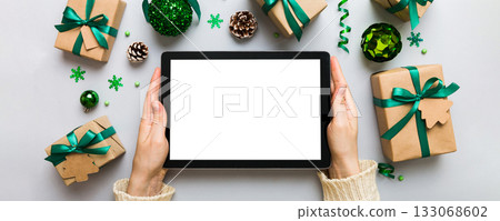 Christmas online shopping from home, female hands holding tablet pc with blank white display top view. woman hand holding tablet with blank screen, Christmas tree and gifts on background Christmas online shopping from home, female hands holding tablet pc with blank white display top view. woman hand holding tablet with blank screen, Christmas tree and gifts on background 133068602