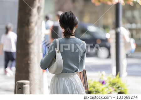 Back view of a young woman standing on a street corner 133069274